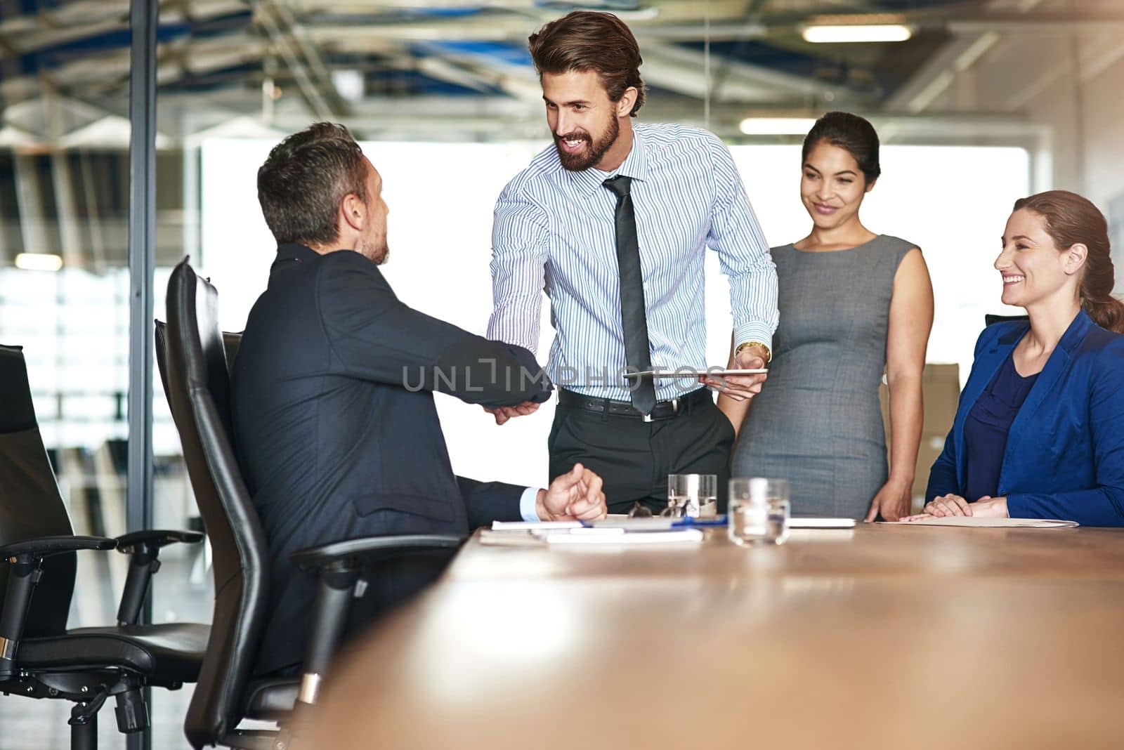 Hes an asset to the team. two businesspeople shaking hands while in a meeting with colleagues in a boardroom. by YuriArcurs