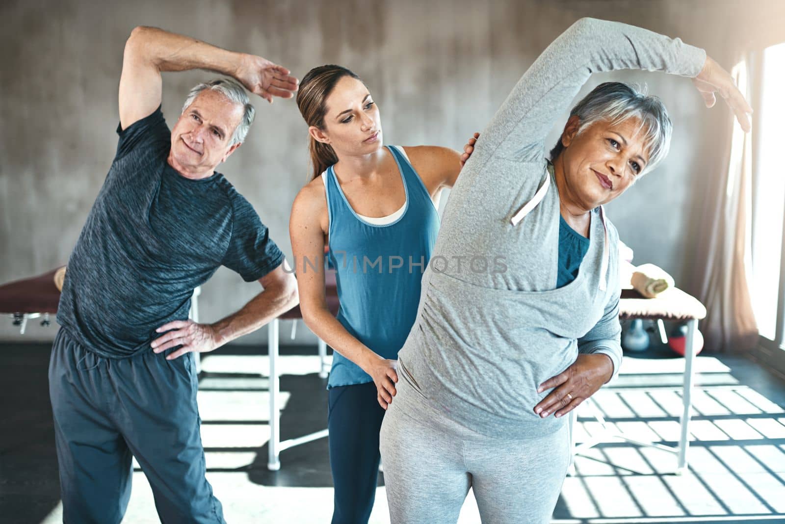 Stay physical, stay flexible. a senior man and woman working out with the help of an instructor. by YuriArcurs