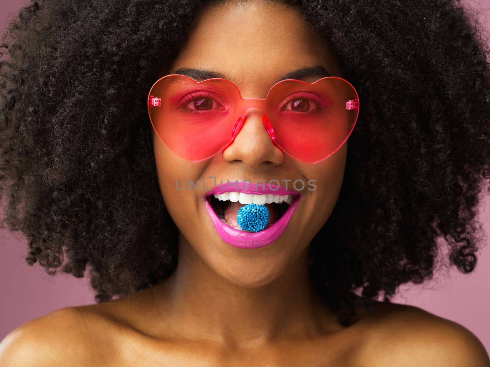 Candy is just dandy. Studio shot of an attractive young woman biting a piece of candy against a pink background. by YuriArcurs