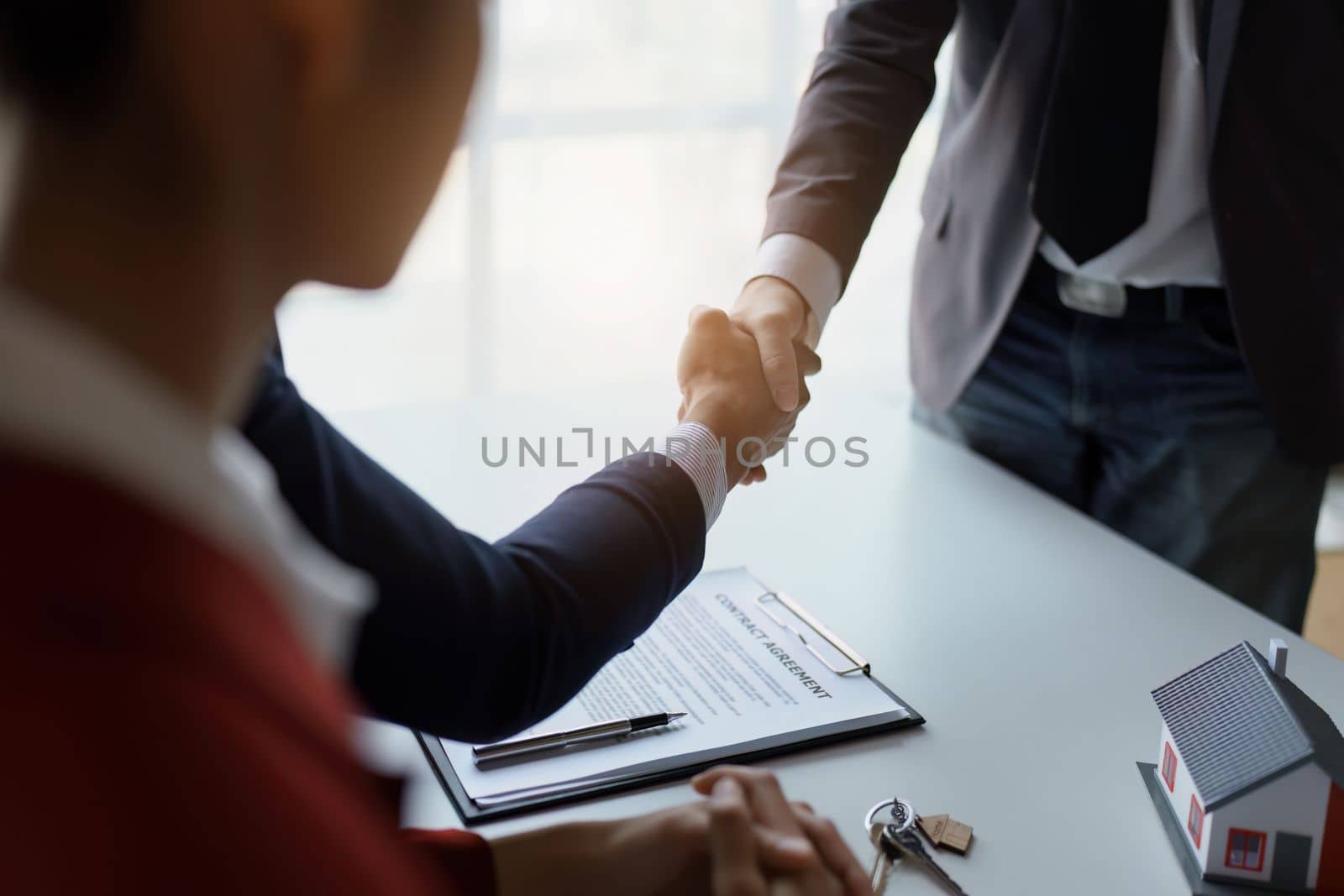 Asian real estate agent shaking hands handing over house and keys to his client's house after client sign contract. by Manastrong