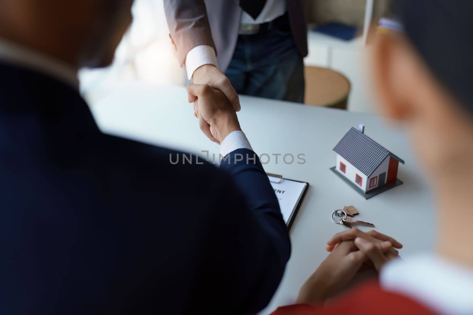 Asian real estate agent shaking hands handing over house and keys to his client's house after client sign contract