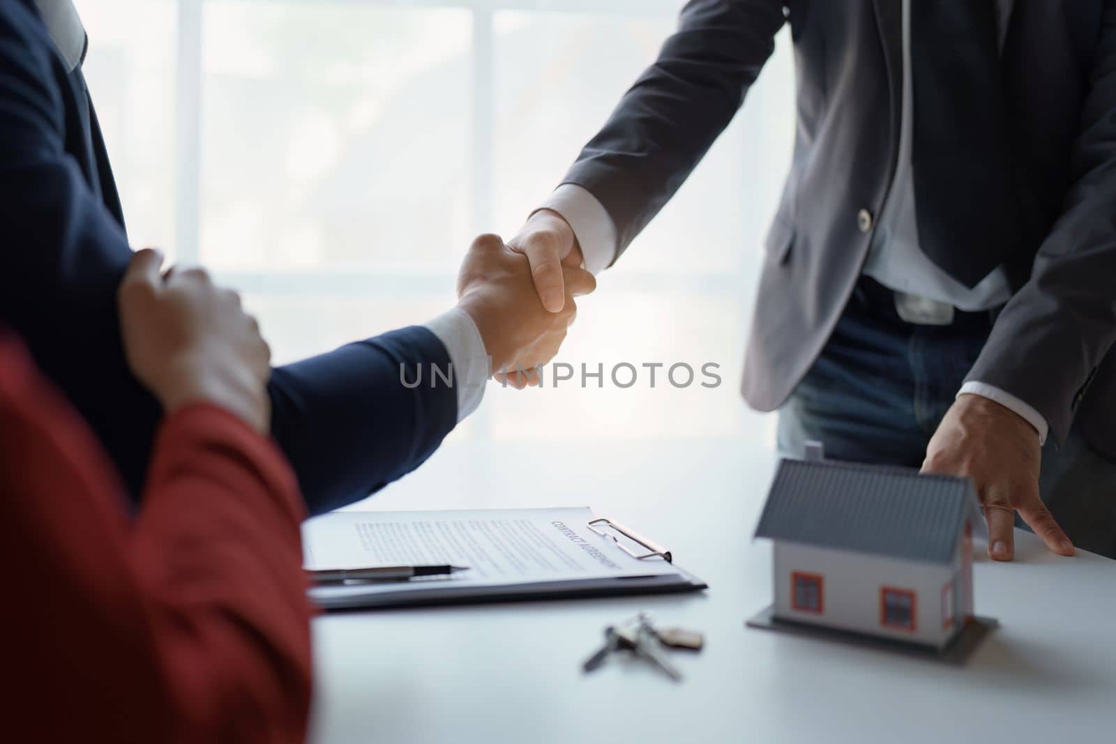 Asian real estate agent shaking hands handing over house and keys to his client's house after client sign contract