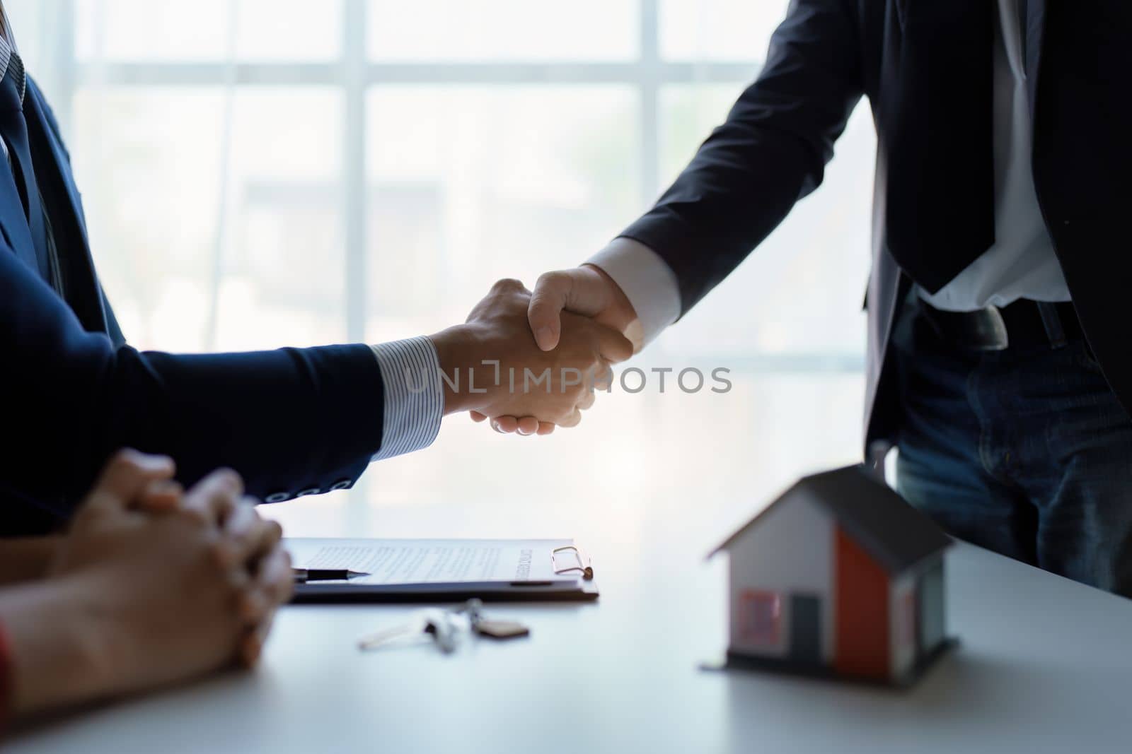 Asian real estate agent shaking hands handing over house and keys to his client's house after client sign contract. by Manastrong