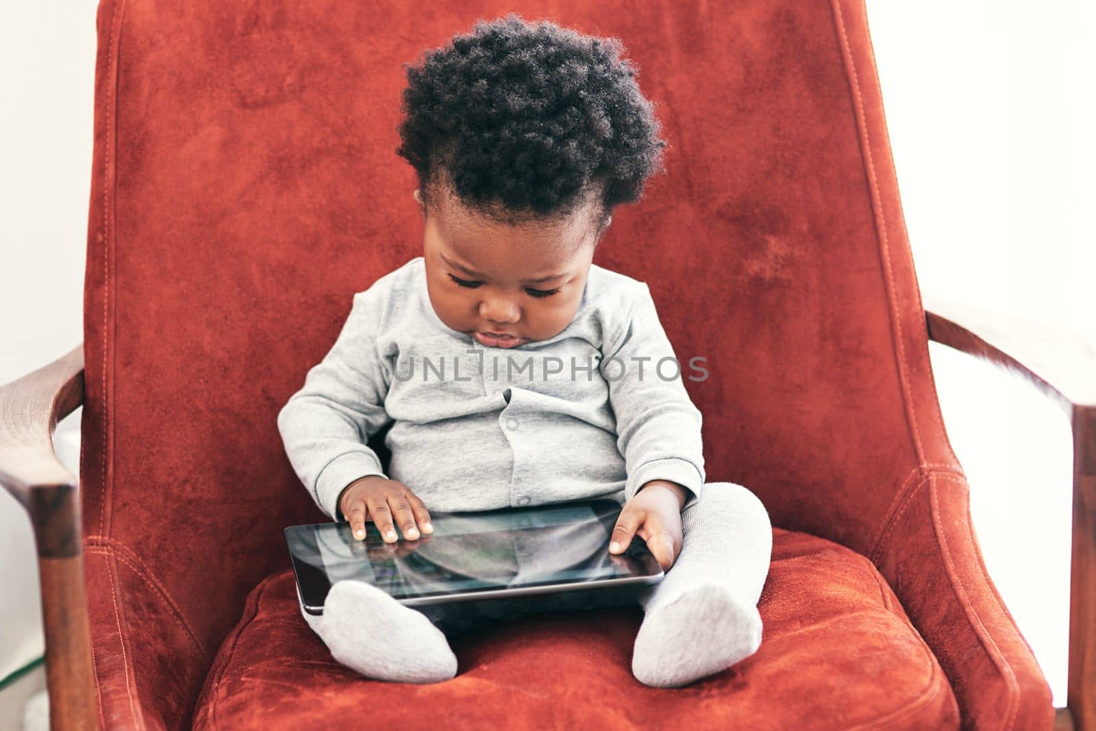 Hes a curious little one. a little baby boy sitting in a chair holding a digital tablet. by YuriArcurs