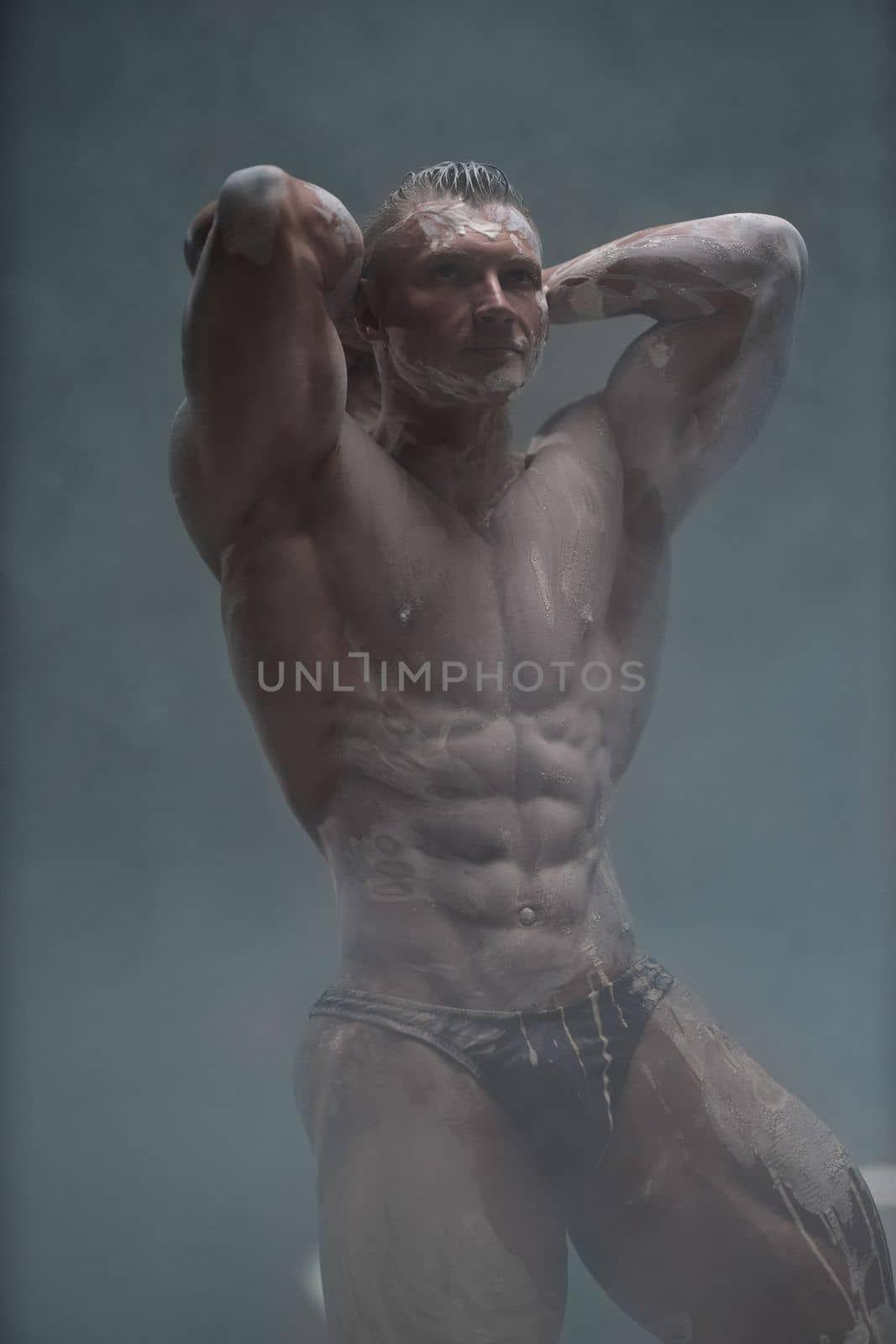 Studio shot of a muscular man. A muscular man shows off his perfect shirtless torso with his hands behind his head. Professional bodybuilder posing concept