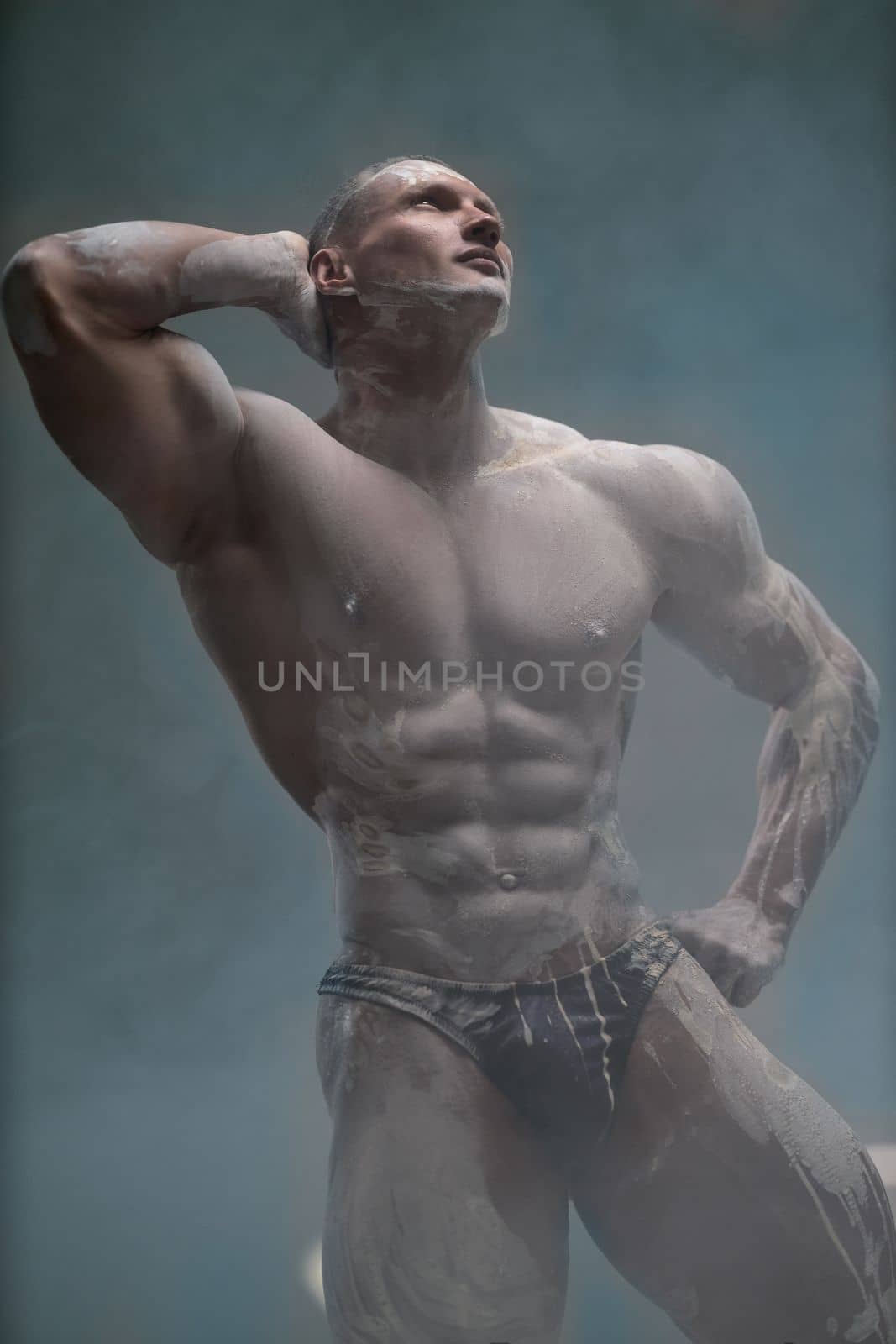 Studio shot of a muscular man. A muscular man shows off his perfect shirtless torso with his hand behind his head. Professional bodybuilder posing concept