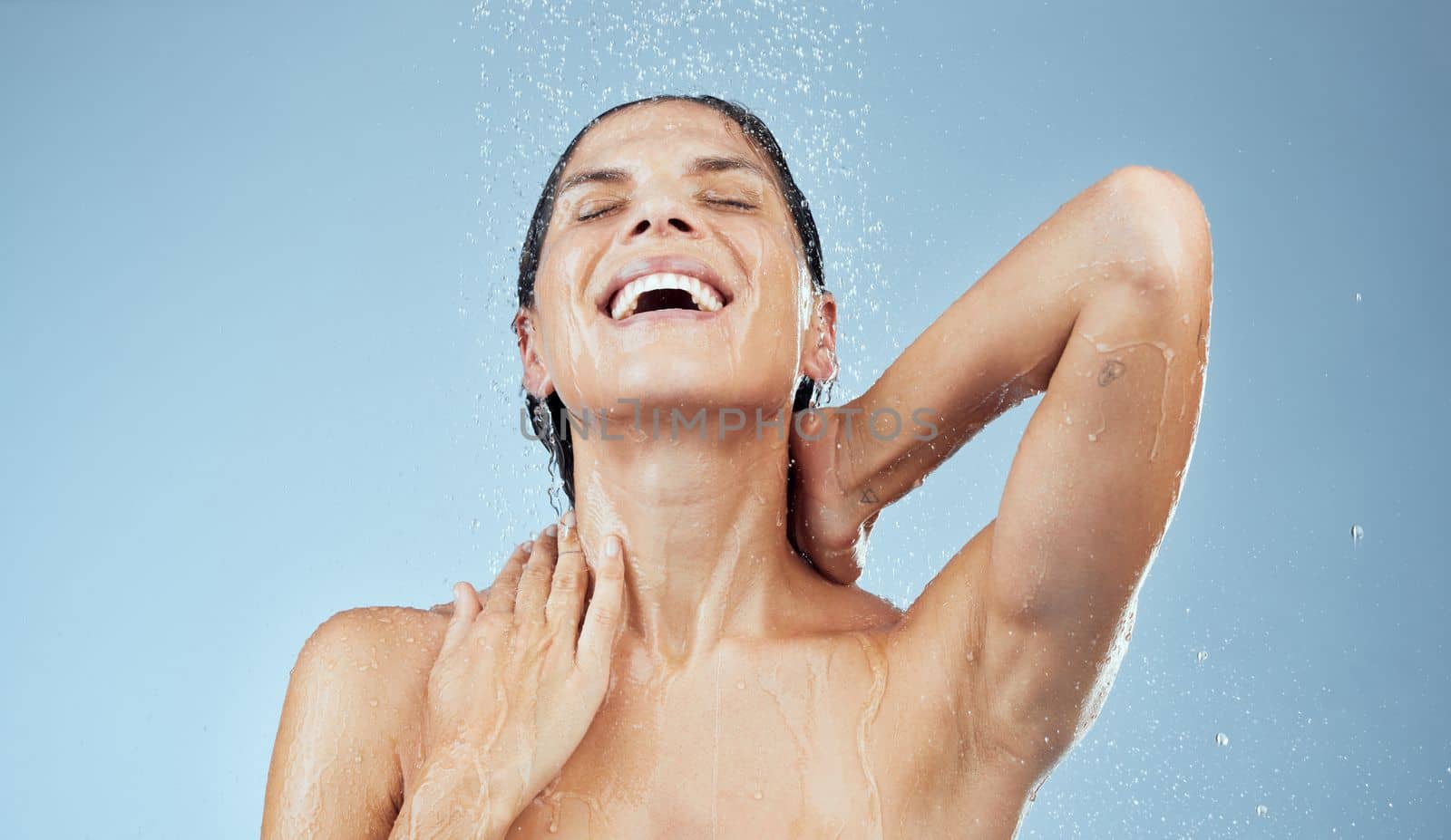 Wash your troubles away. Studio shot of an attractive young woman taking a shower against a blue background. by YuriArcurs