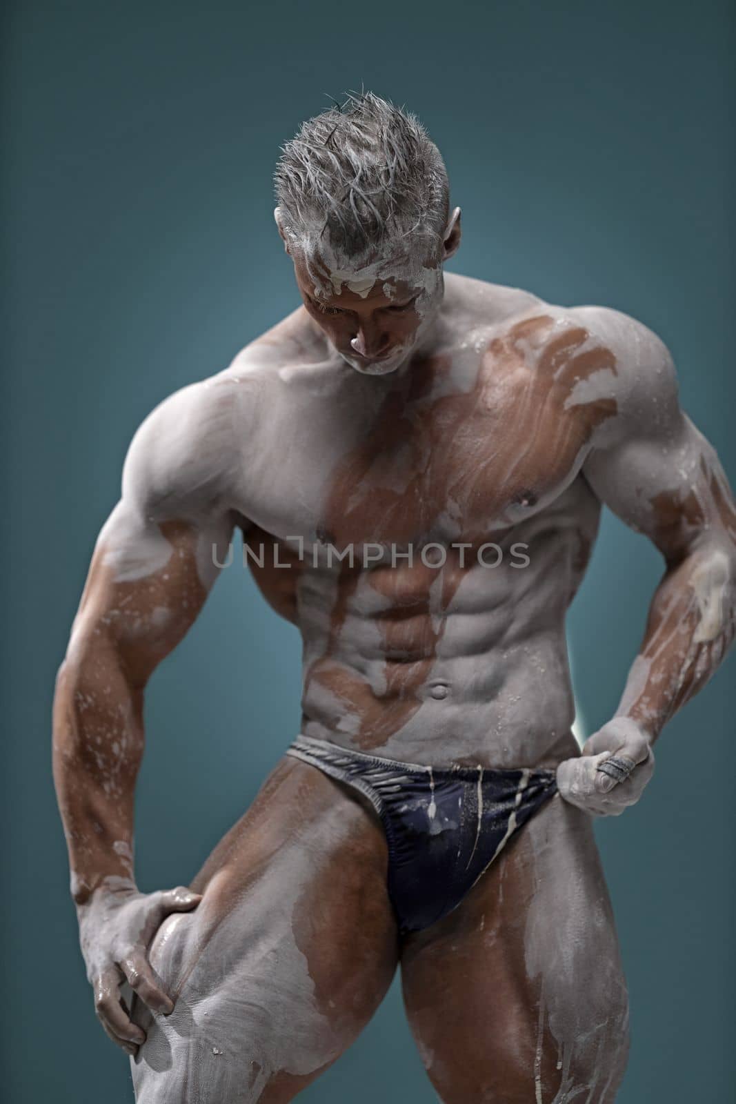 Studio shot of a muscular man. Young handsome athletic caucasian guy with beautiful naked torso looking away while posing shirtless isolated over grey background. Sports workout concept