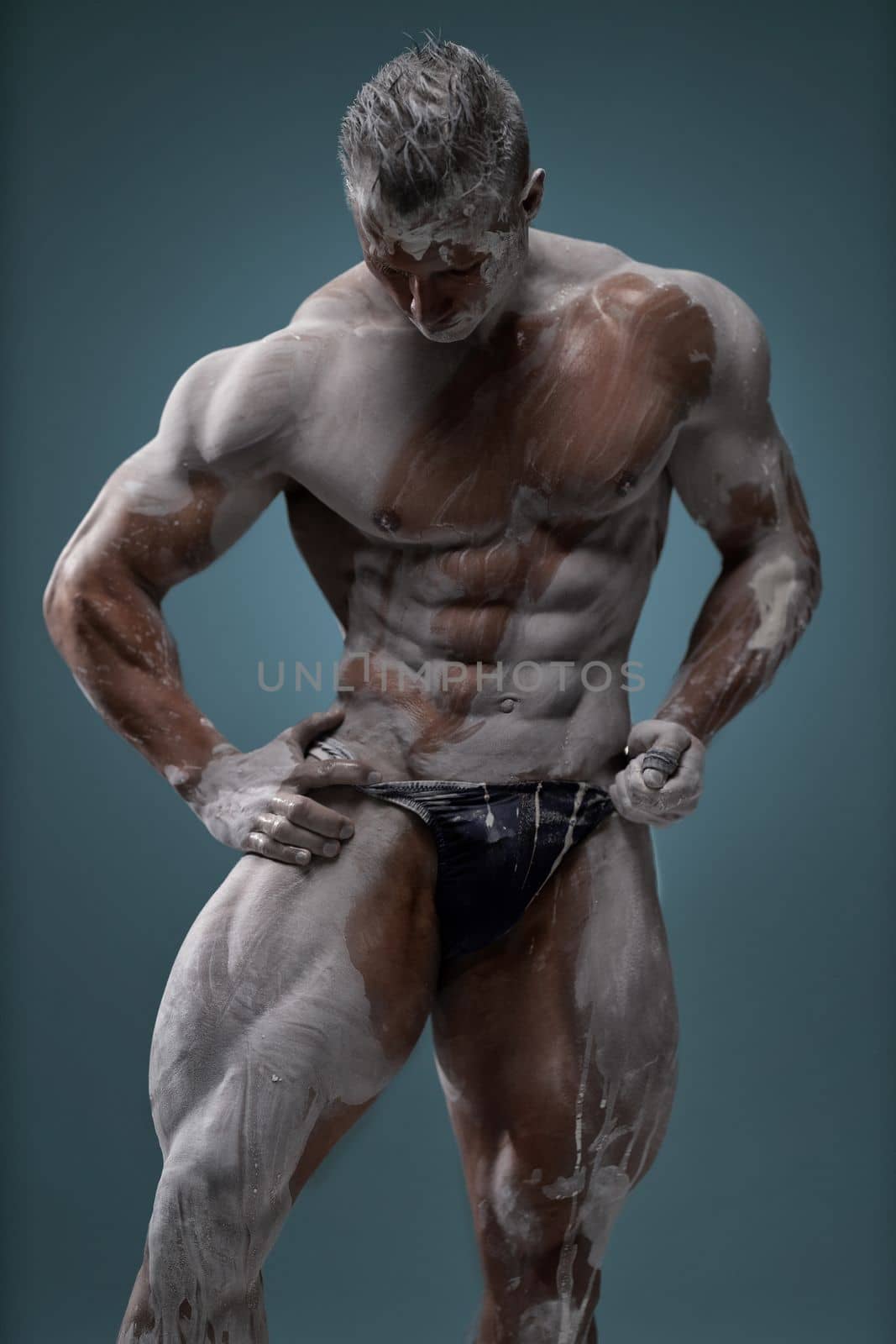 Studio shot of a muscular man. Young handsome athletic caucasian guy with beautiful naked torso looking away while posing shirtless isolated over grey background. Sports workout concept