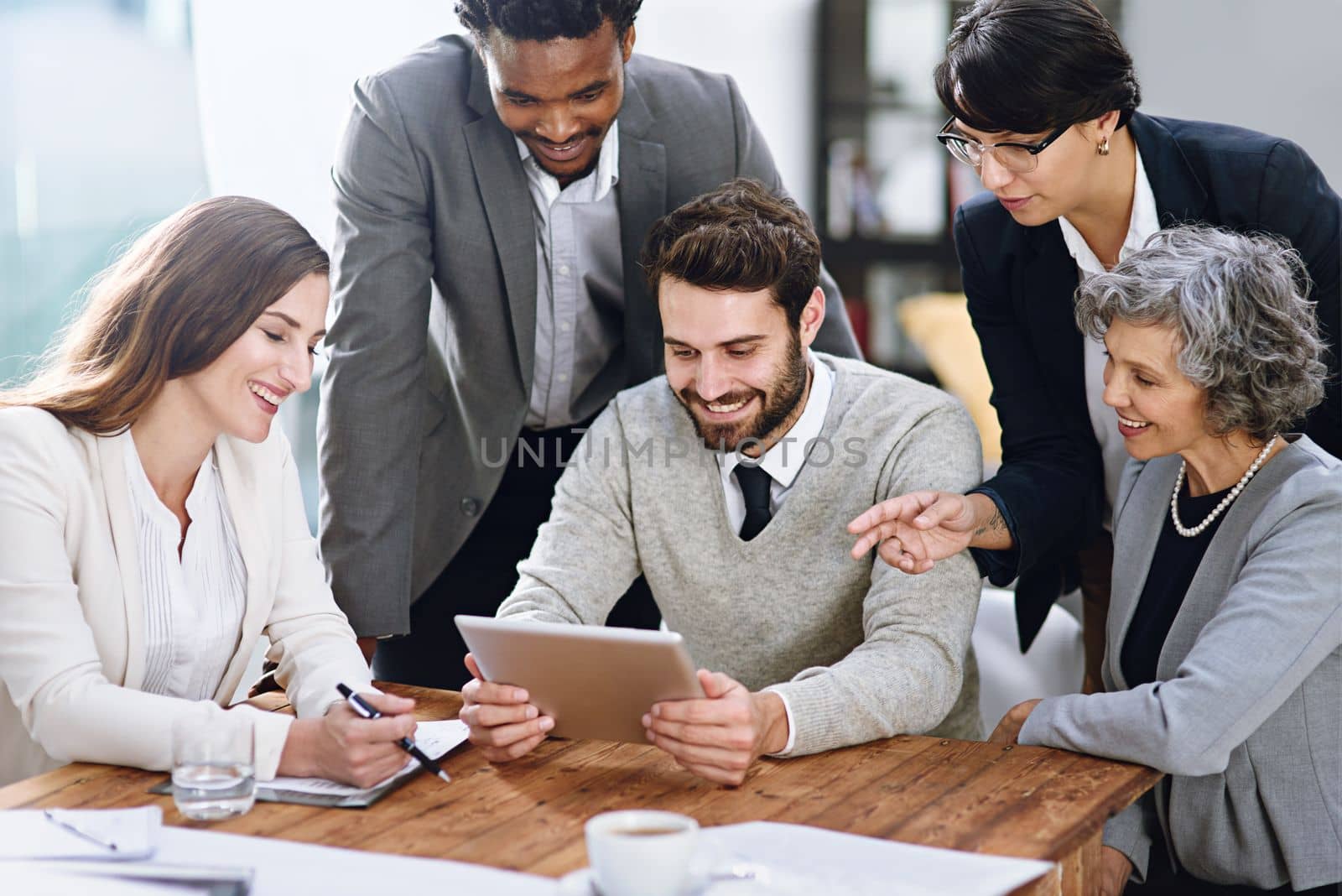 Taking charge of business together. a group of businesspeople working together on a digital tablet in an office