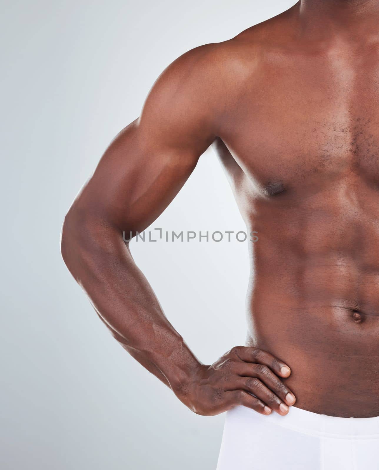 Closeup of one African American fitness model posing topless in a underwear and looking muscular. Confident black male athlete isolated on grey copyspace in a studio wearing boxers showing his sixpac.