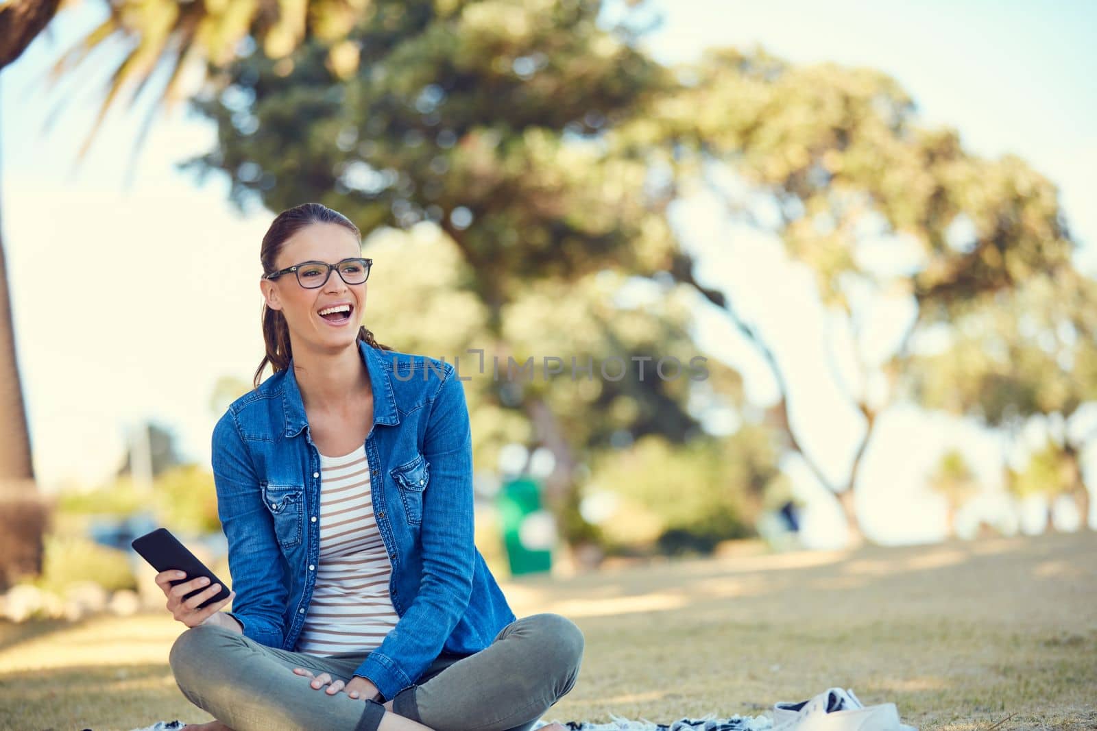 The best days are spent doing what you love. an attractive young woman using a mobile phone while relaxing in the park. by YuriArcurs