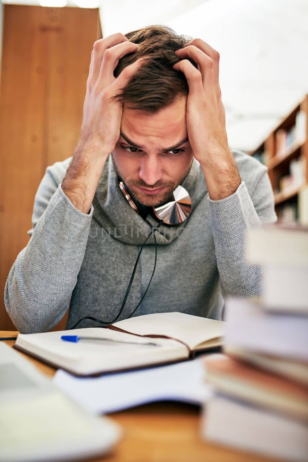 Its too much work for his brain to absorb. a university student looking stressed out while working in the library at campus. by YuriArcurs