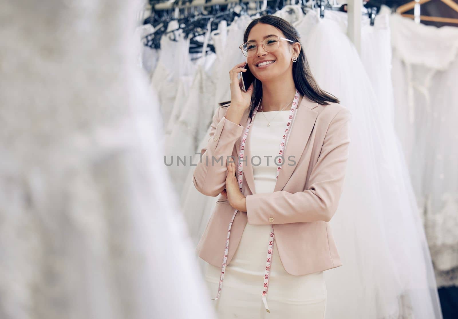 Our dresses will make you feel like the beautiful bride you are. a seamstress talking on her cellphone while working in her boutique. by YuriArcurs