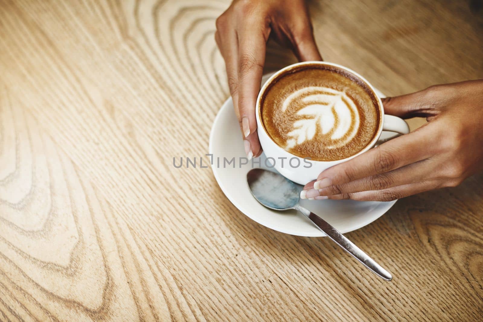 Mmm... coffee. High angle shot of an unrecognizable woman holding a cup of coffee decorated with froth art