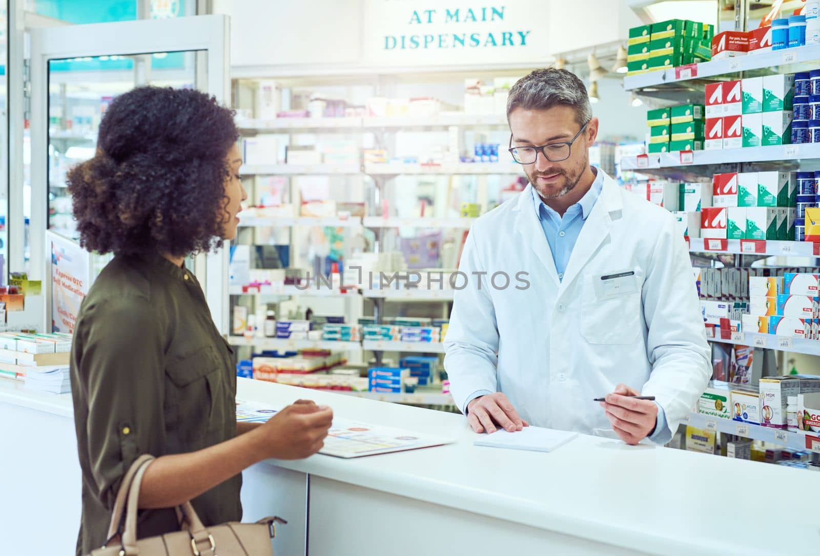 Filling out her prescription. a handsome mature male pharmacist helping a female customer in the pharmacy