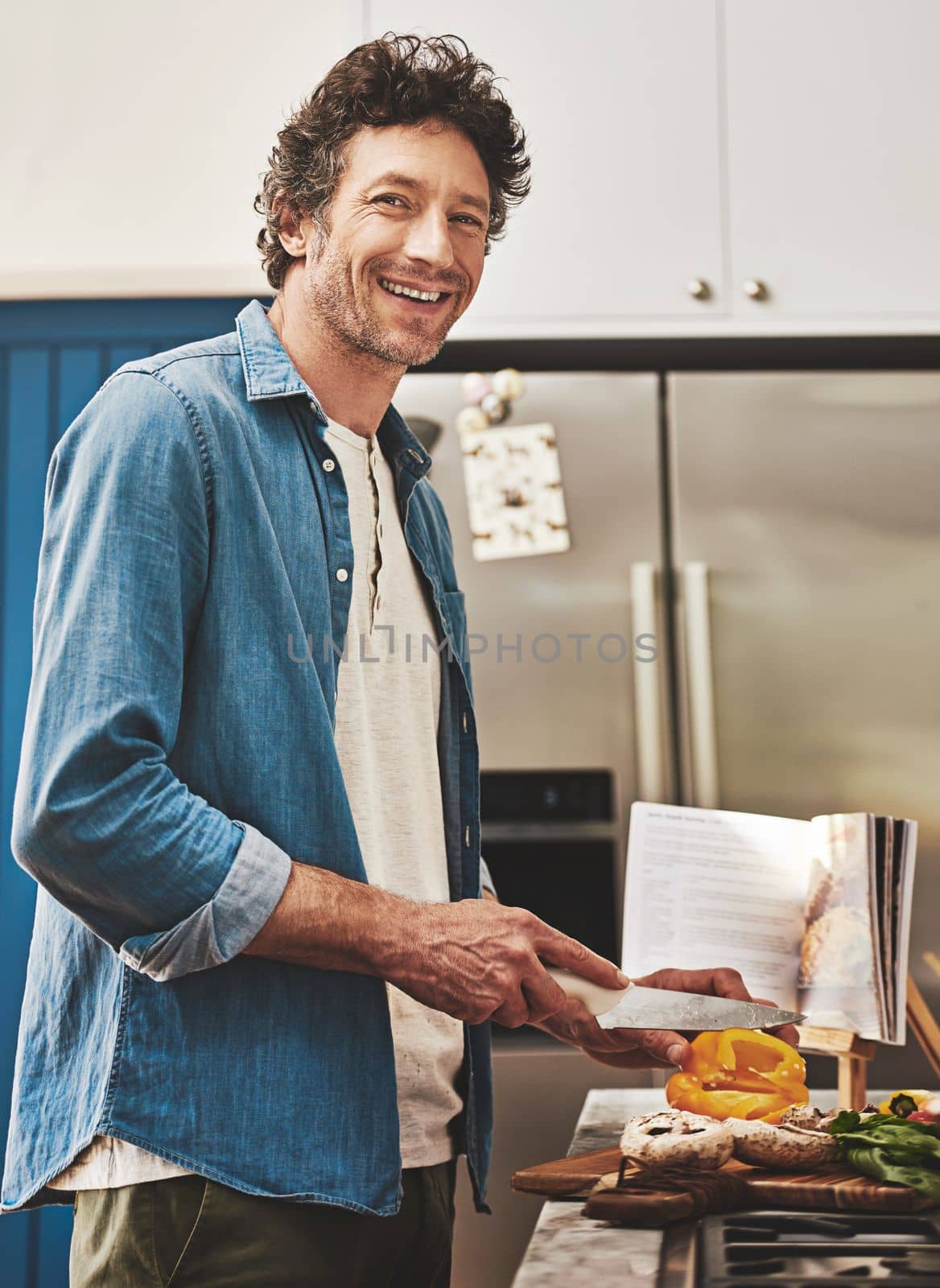 When you eat better, you feel better. Portrait of a happy bachelor chopping vegetables in his kitchen. by YuriArcurs