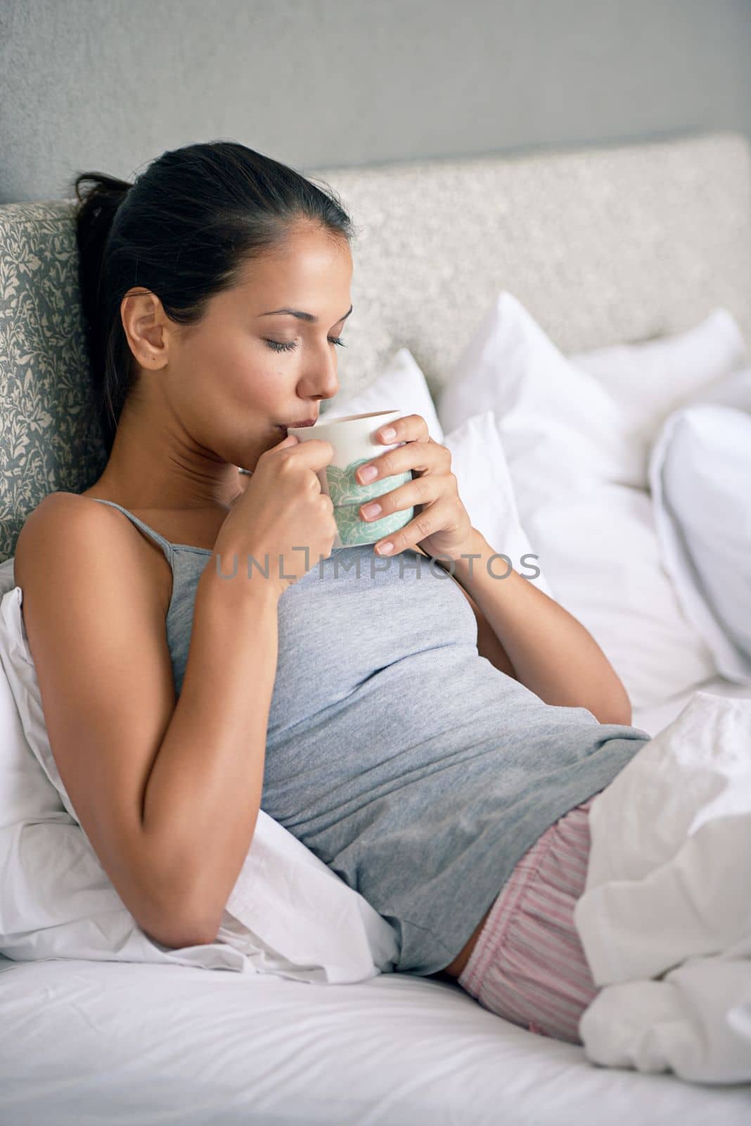 Taking that first sip of fresh coffee in the morning. a young woman drinking coffee while sitting in bed. by YuriArcurs