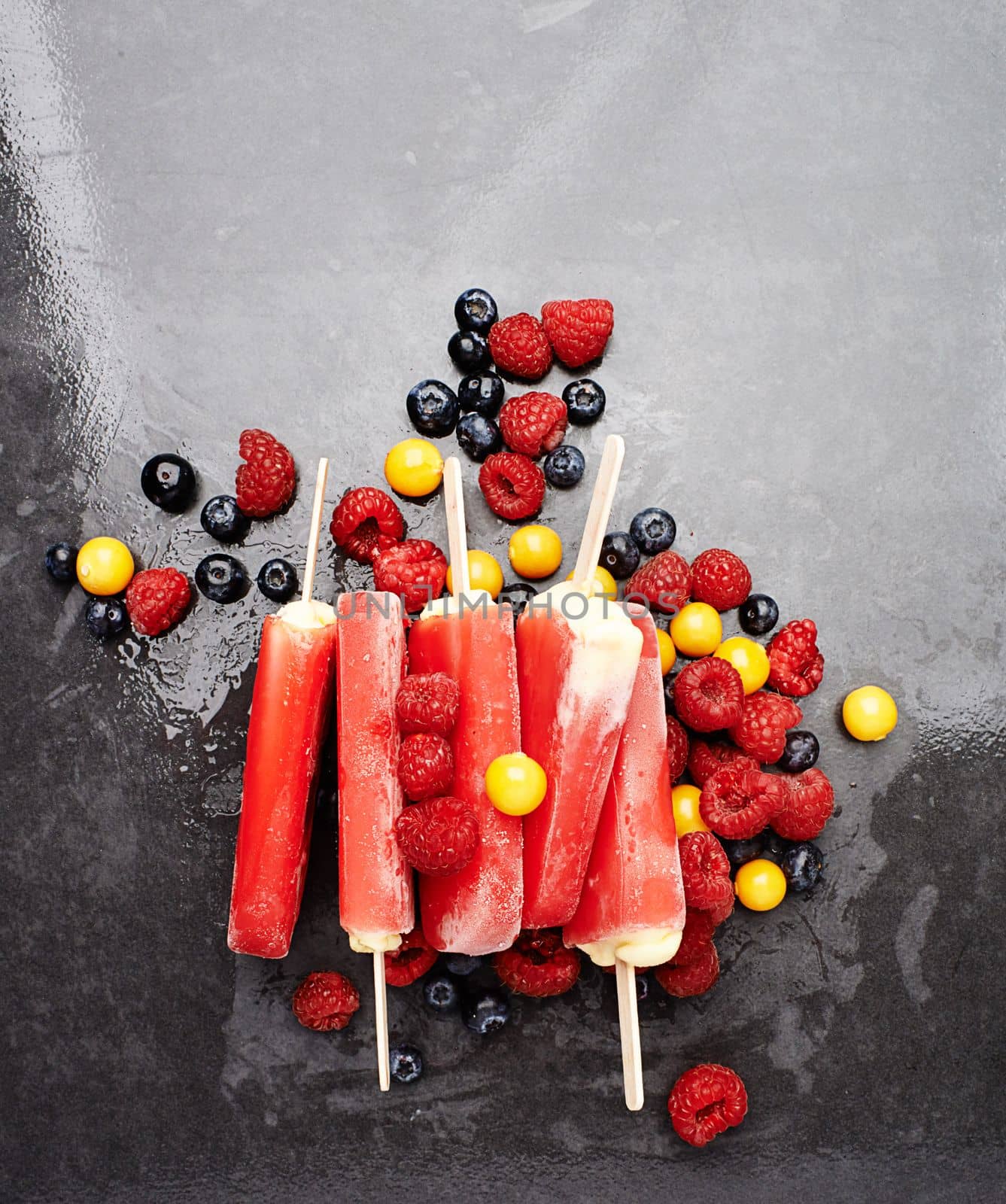 Melt in your mouth goodness. Studio shot of berry ice lollies surrounded by an assortment of berries. by YuriArcurs