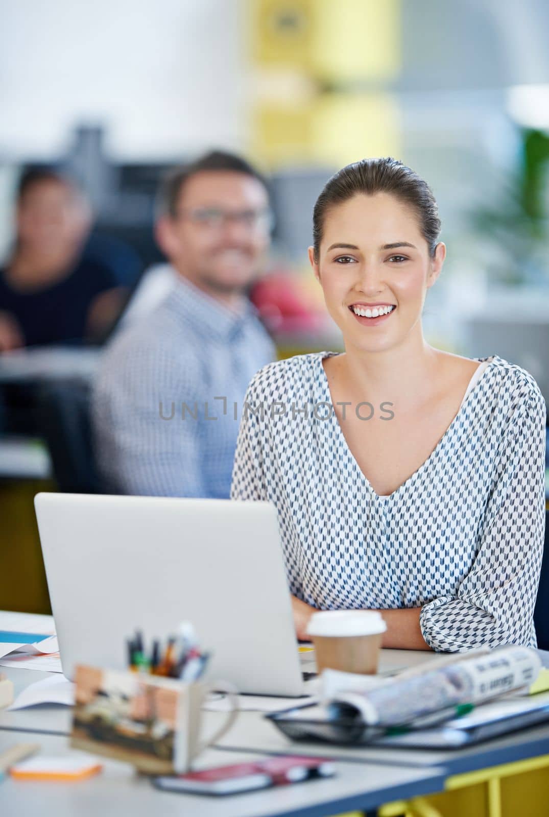 Follow your career dreams. Portrait of a designer sitting at her desk working on a laptop with colleagues in the background