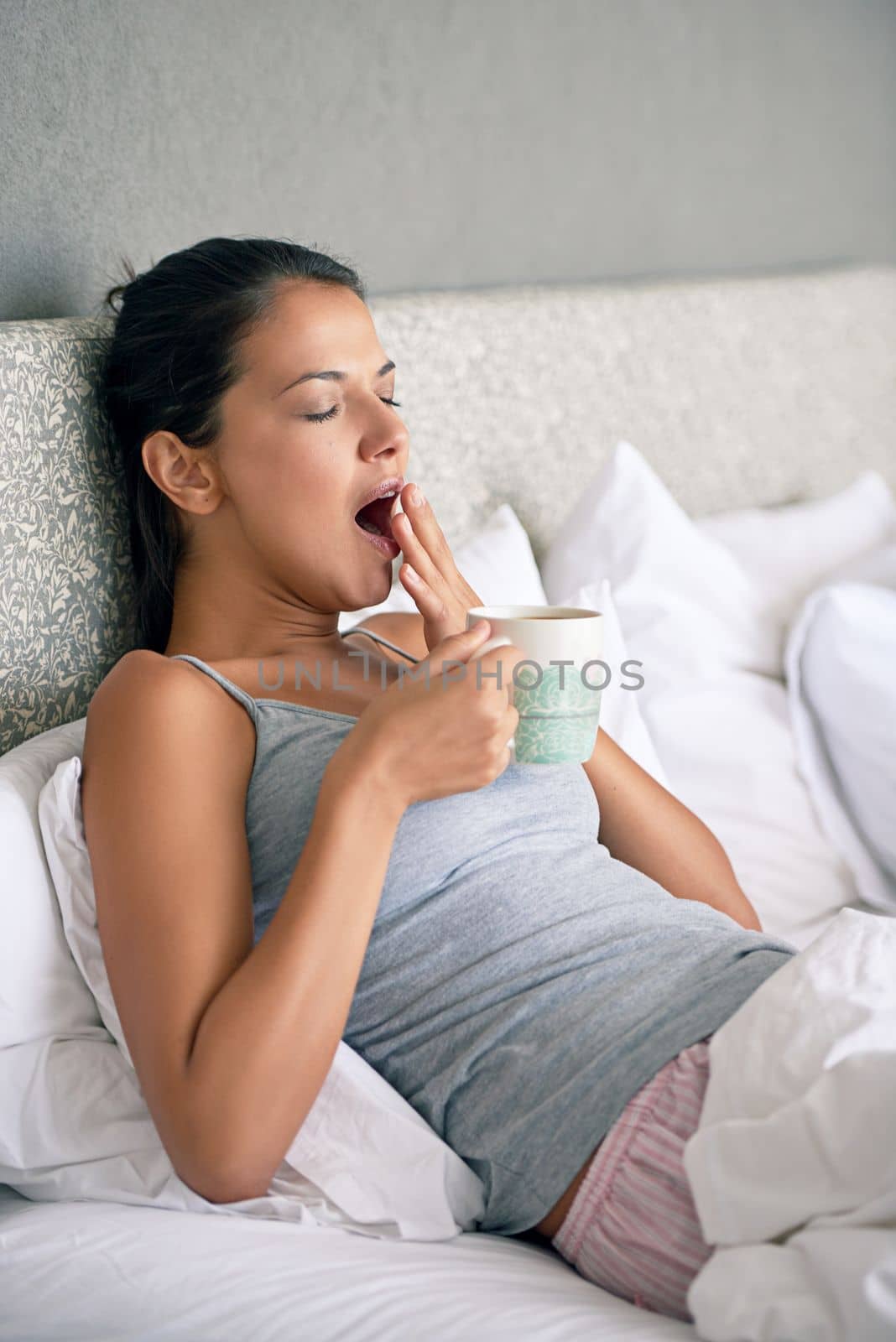 Theres nothing like a little coffee to wake you up. a young woman drinking coffee while yawning in bed