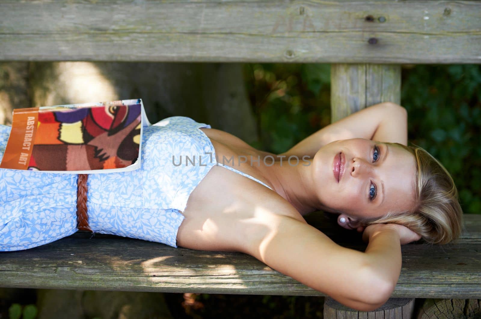 Ruminating on a great read. a beautiful young woman with a book lying down on a bench outside