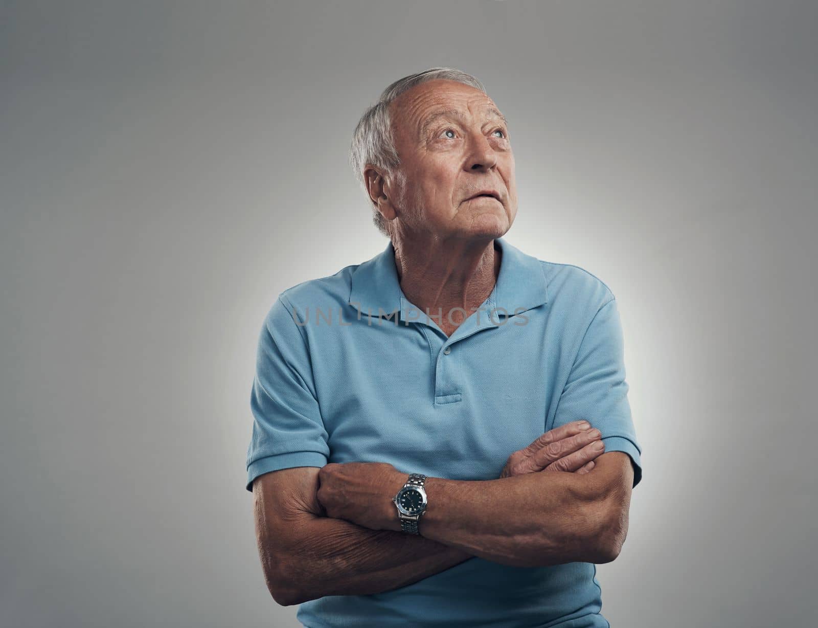 What is that light over there. an older man with his arms crossed looking off into the distance in a studio against a grey background. by YuriArcurs