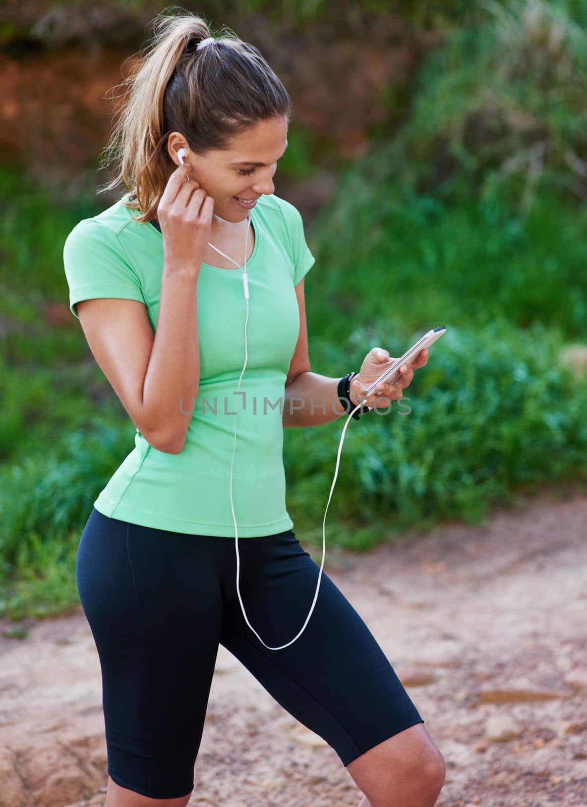 Choosing some tunes for the trail. a young woman listening to music while exercising in the outdoors. by YuriArcurs