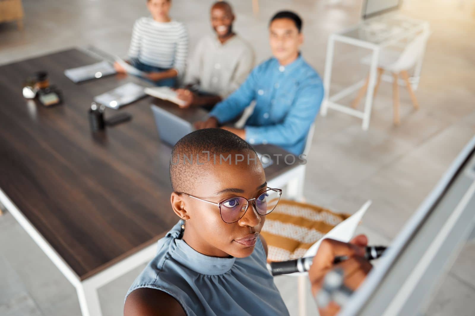 Group of diverse businesspeople having a meeting in an office at work. Young african american businesswoman writing an idea on a whiteboard in a boardroom with colleagues. Businesspeople planning tog by YuriArcurs