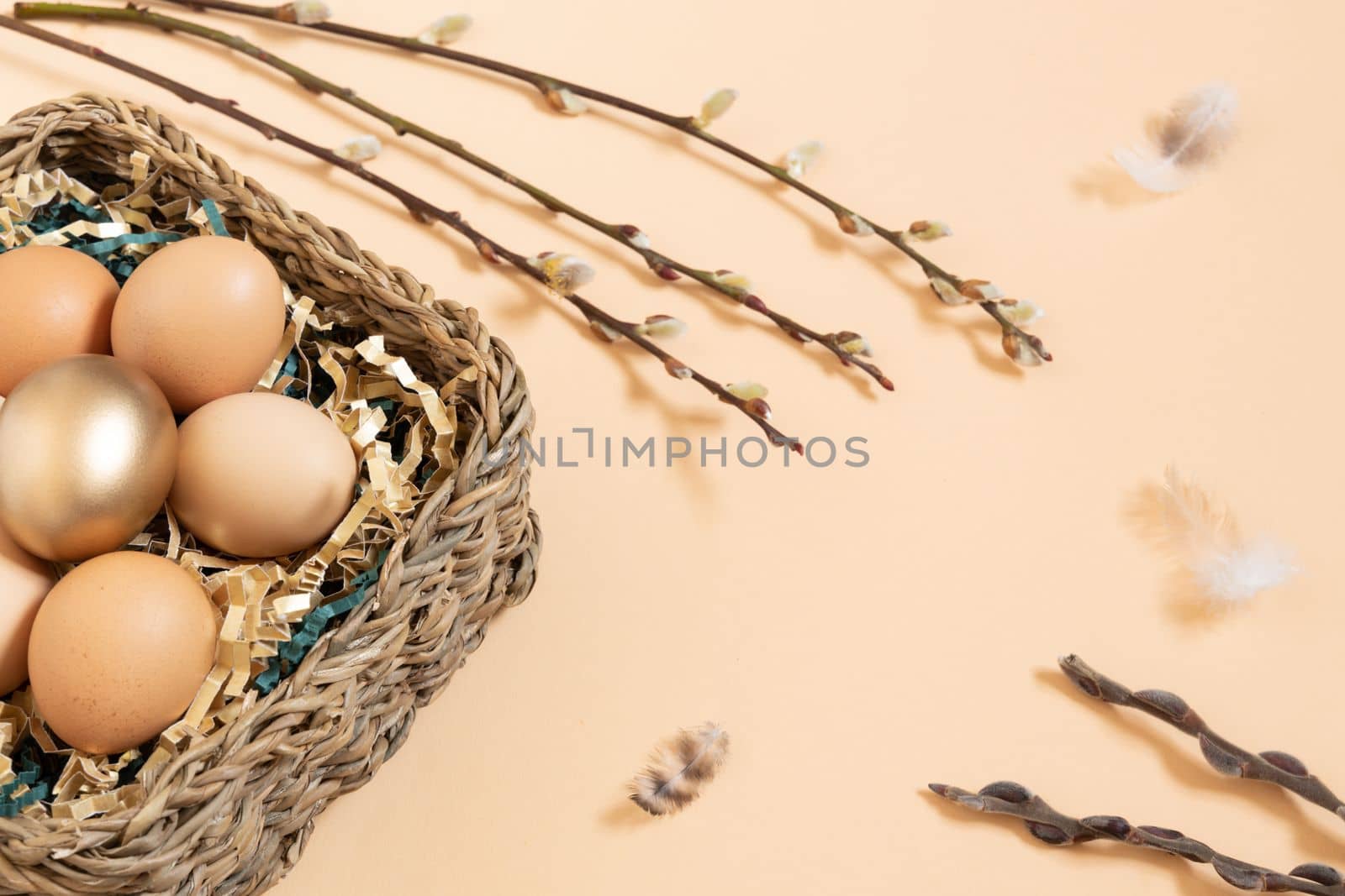 Easter eggs natural and gold in basket with paper filler . Branch of willow catkinsan feather. Light pastel orange background with copy space. by Ri6ka