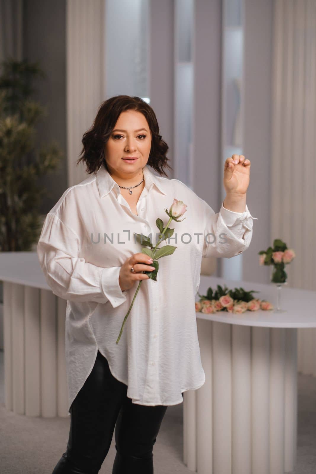 An adult woman in a white shirt holds one rose in her hands while standing in the interior. Pink roses by Lobachad