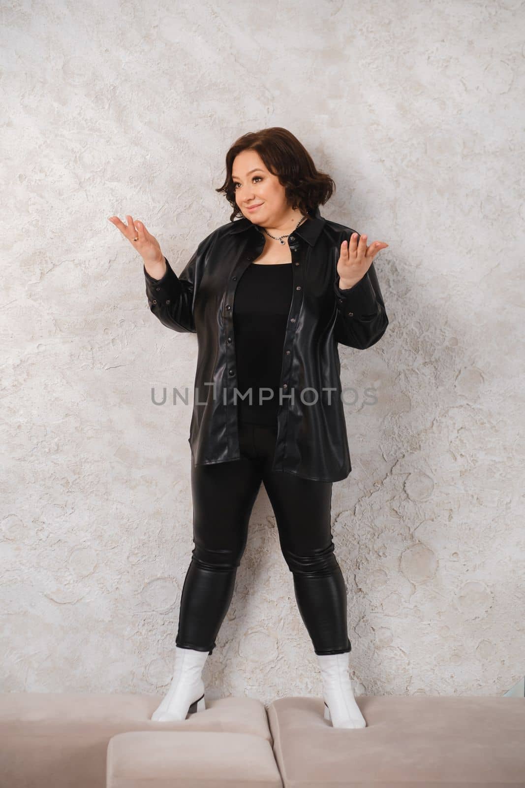 An adult woman in black leather clothes poses against a gray studio wall by Lobachad