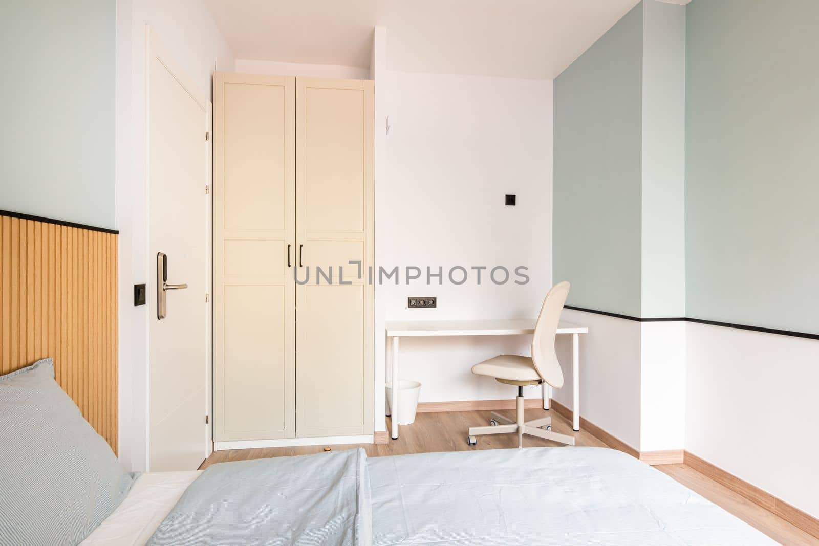 A bright room with walls in a soft mint color, a bed for two people, a work area with a table and a chair, a wardrobe with beige wooden doors. Door with electronic combination lock. by apavlin