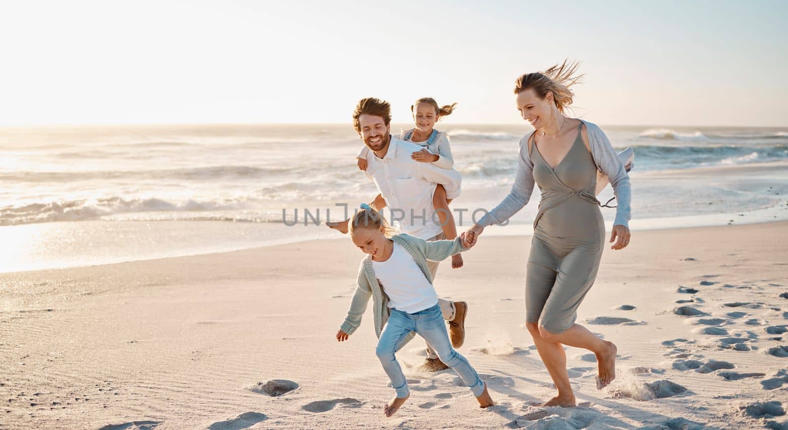 Carefree family playing on the beach together. Happy family on vacation by the ocean together. Little girls playing with their parents on holiday. Caucasian family bonding on the beach.