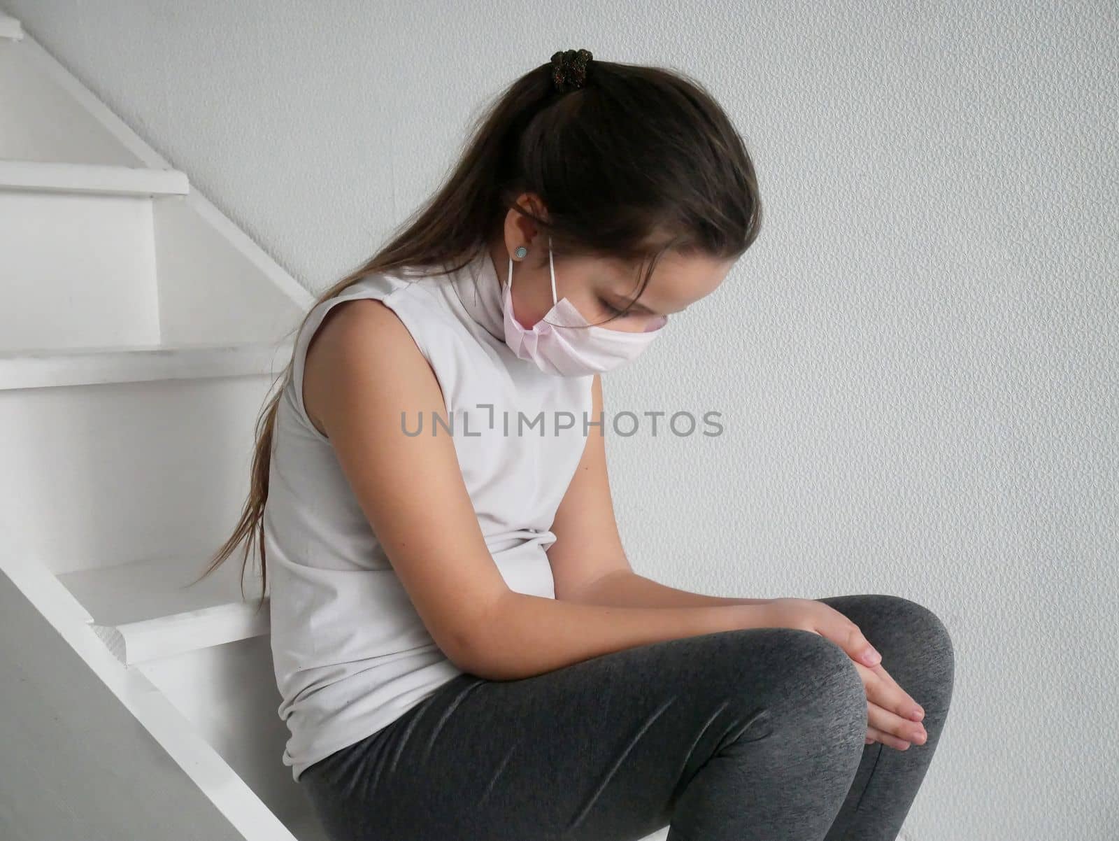 Student girl wearing a mask seating on stairs after COVID-19 quarantine and lockdown, sad and tired of not going to school with her friends. by Jyliana