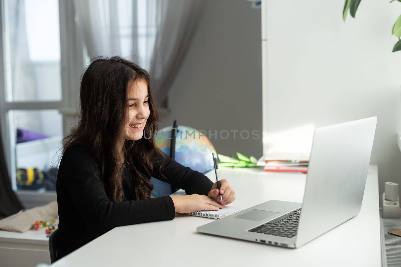 Smiling young teen schoolgirl involved in video web camera call on computer with teacher, listening distant educational lecture in online classroom. homeschooling concept