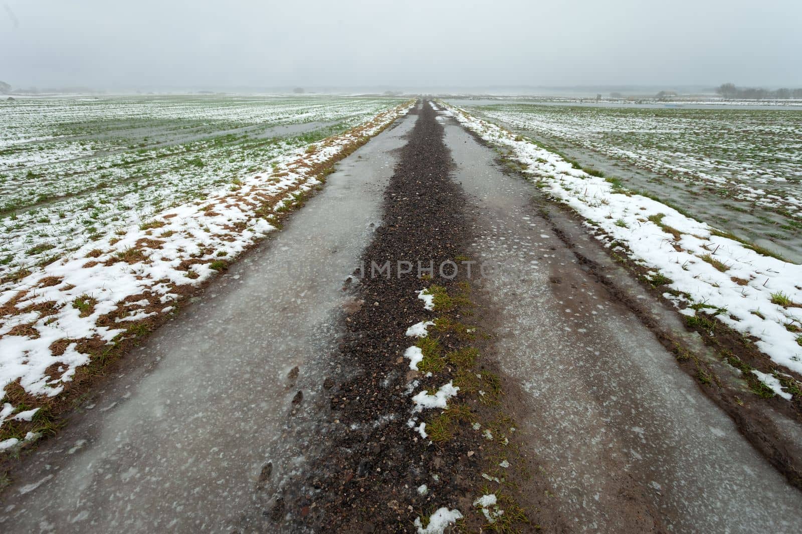 Icy dirt road through fields with snow and water, view on a foggy day, eastern Poland by darekb22