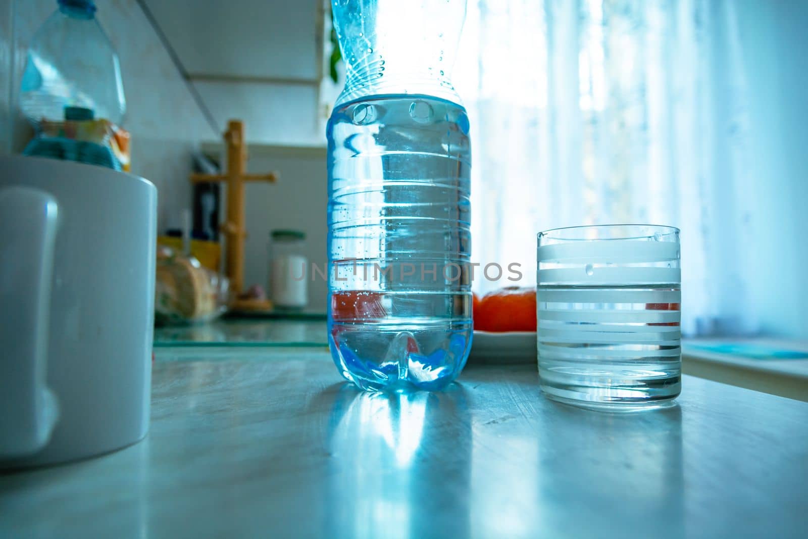 A plastic water bottle and an empty glass standing on the kitchen counter