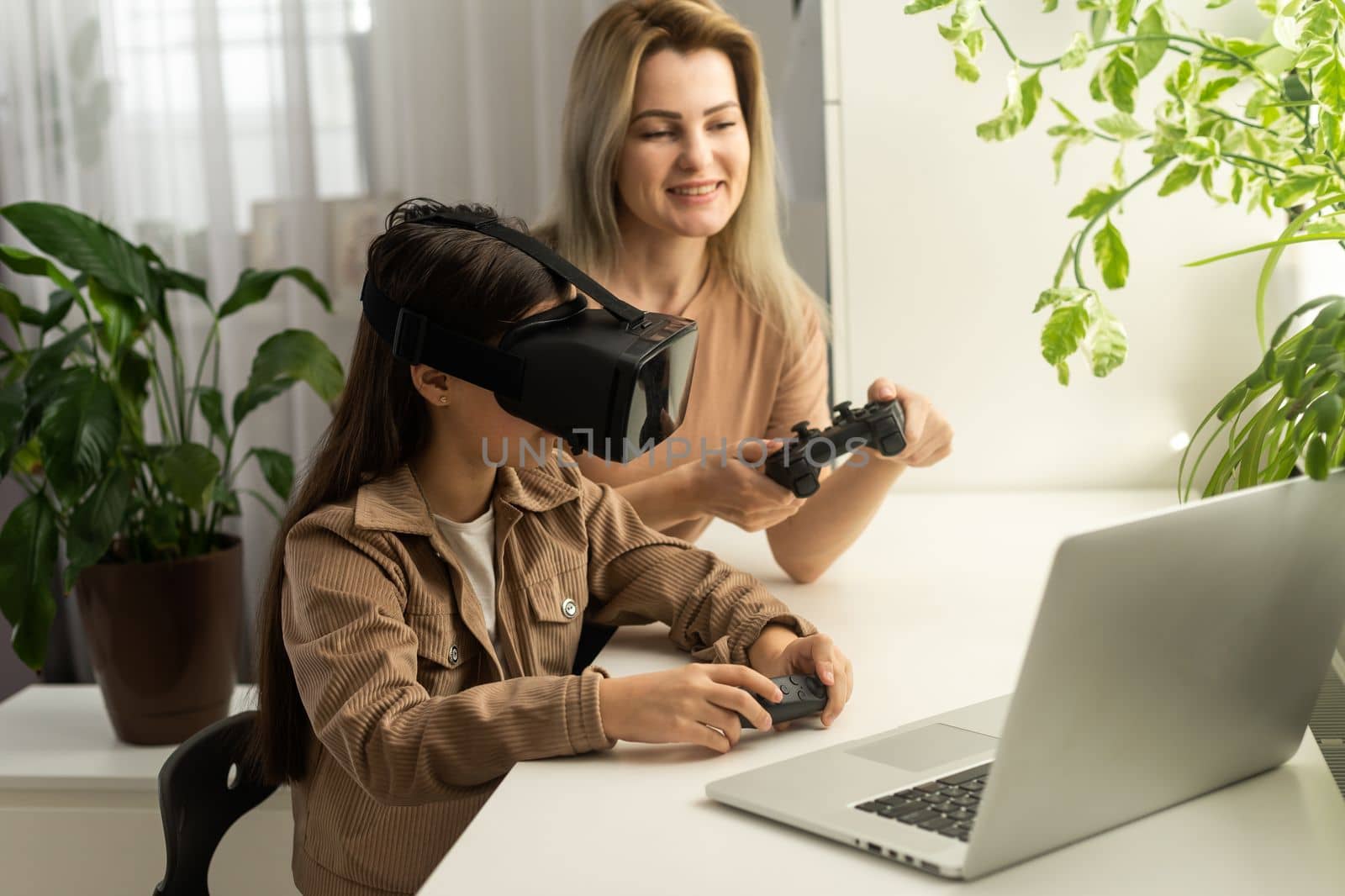 Families and new technologies. Smiling work-at-home mother sitting with daughter wearing vr helmet exploring virtual reality. Curious child teen girl testing AR technology for education by Andelov13