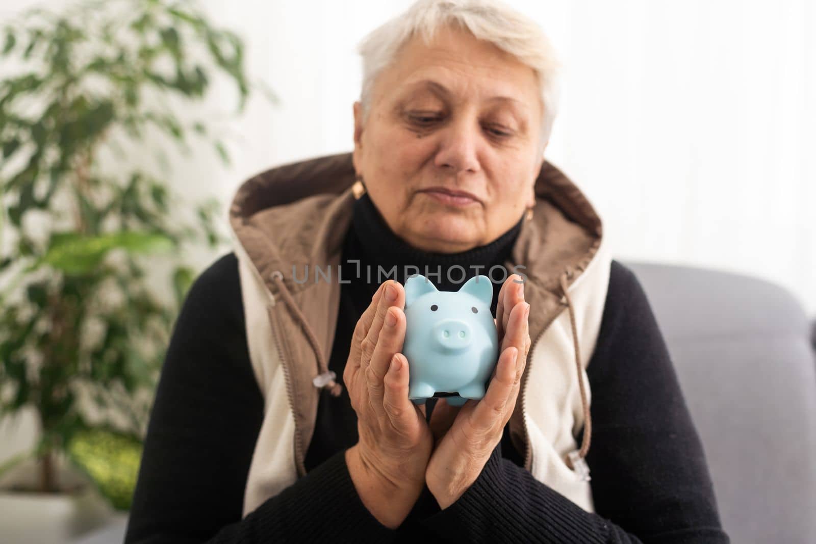 Close-up shot of elderly woman holding pig money-box. Senior woman hands holding a piggybank. Concept of saving money for old age. by Andelov13