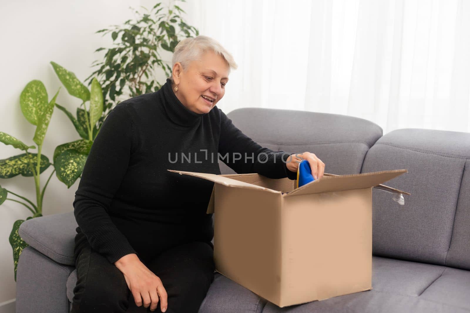 Elderly woman unpacking things in new house. Female hands opening cardboard box. Real estate, purchase, moving concept