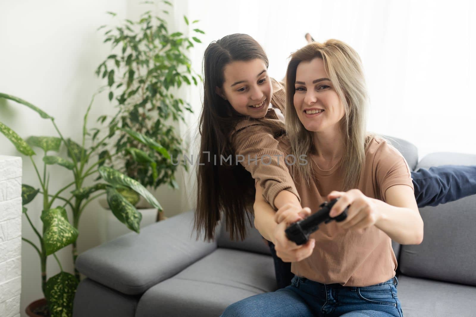 good relationship cute little girl with young mother using joystick playing video game sitting together in living room wooden floor enjoying family holiday.