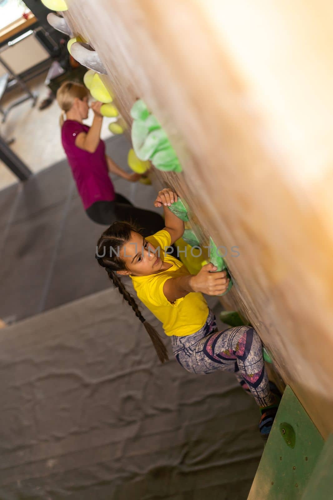 Young female bouldering instructor helping boy climb artificial wall.