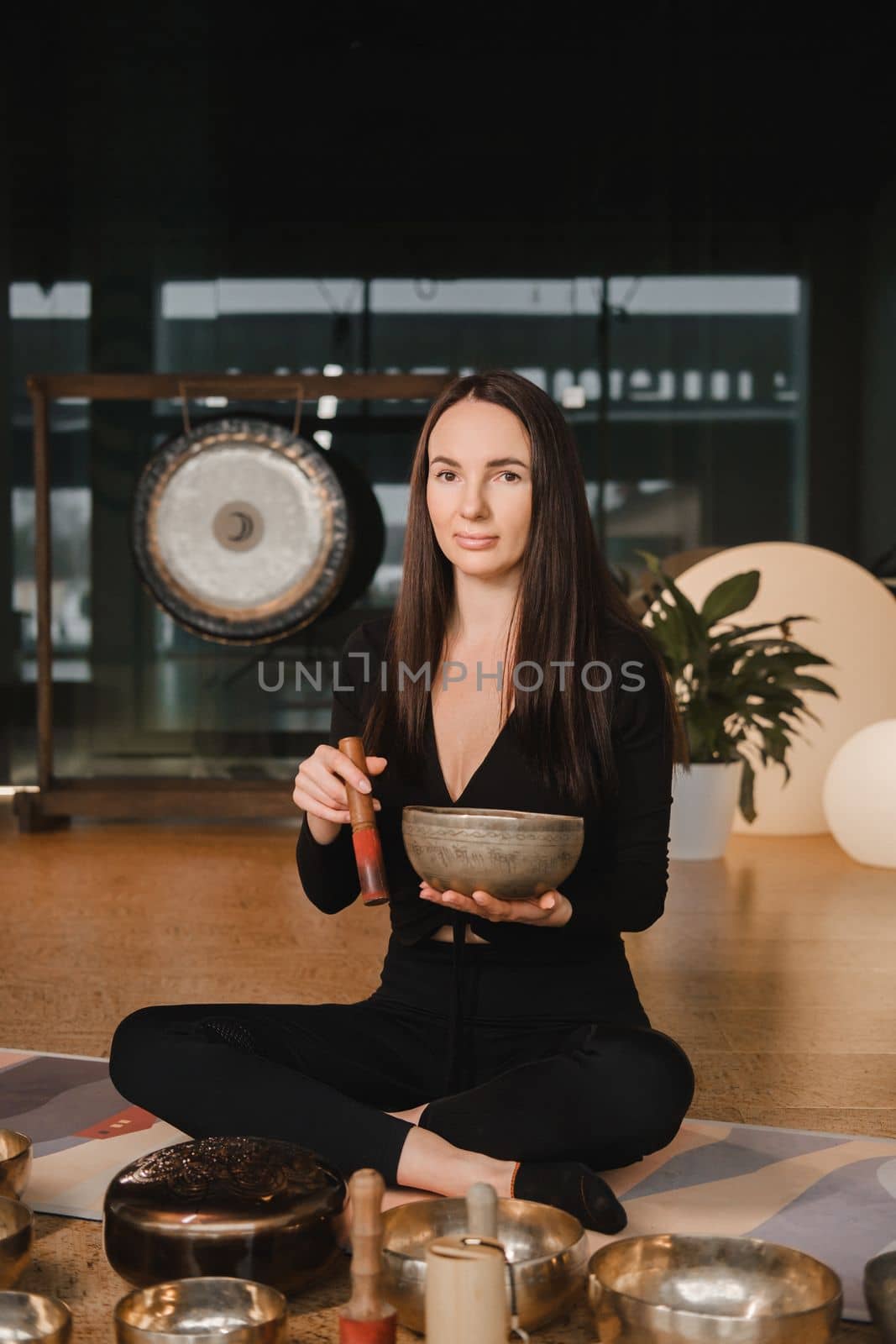 A woman in the lotus position using a singing bowl indoors . Relaxation and meditation. Sound therapy, alternative medicine. Buddhist healing practices by Lobachad