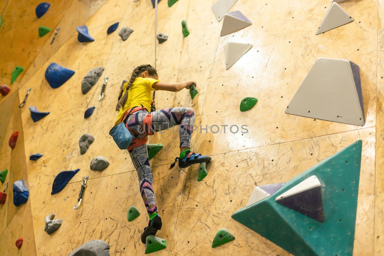 little girl climbing a rock wall indoor.