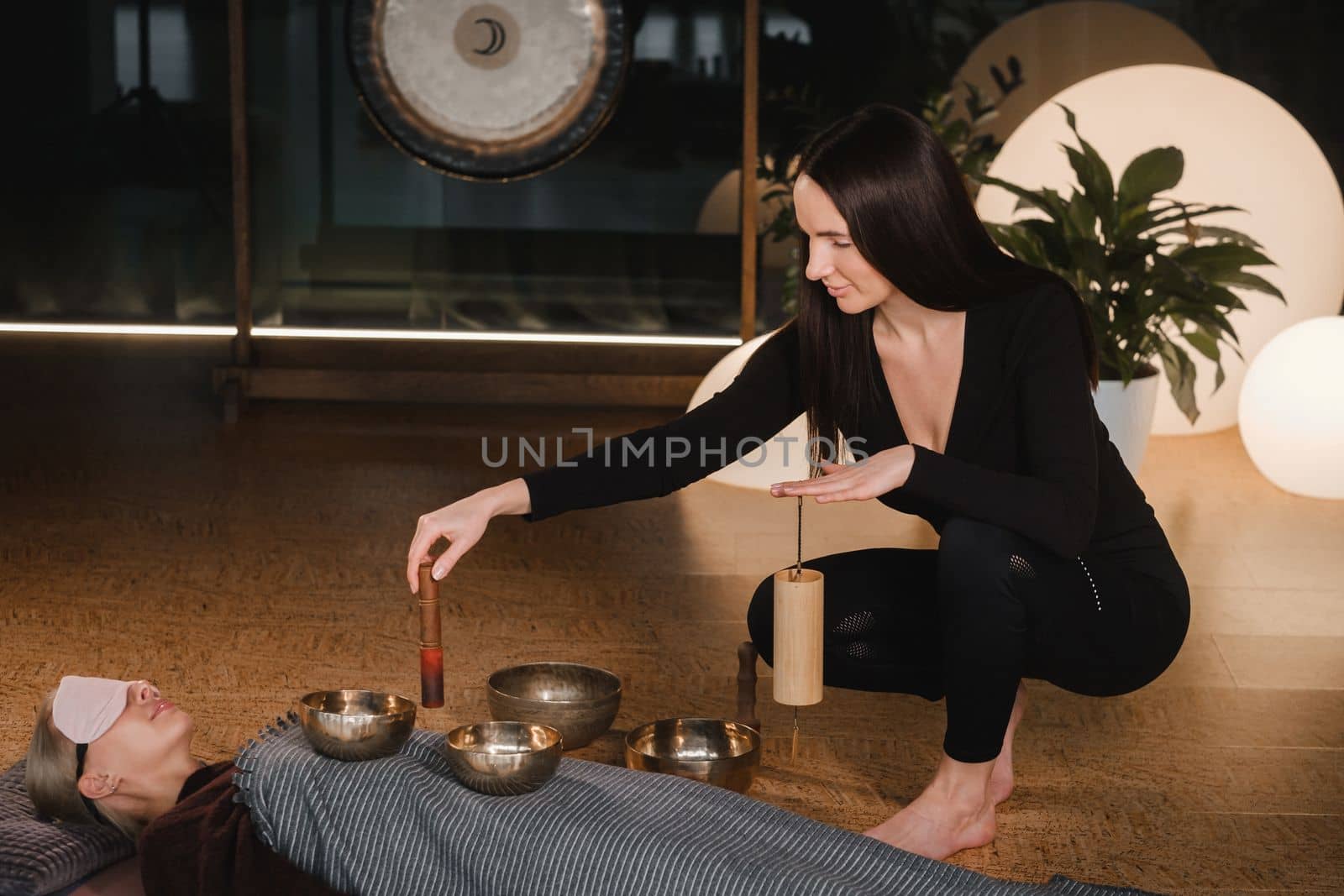 A young beautiful woman is doing a massage with singing bowls and a koshi bell to another girl. Sound therapy.