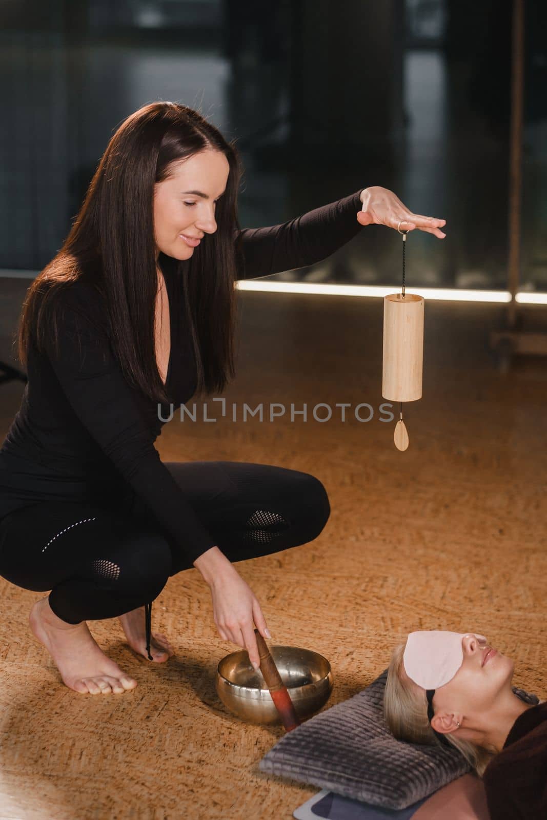 A young beautiful woman is doing a massage with singing bowls and a koshi bell to another girl. Sound therapy by Lobachad