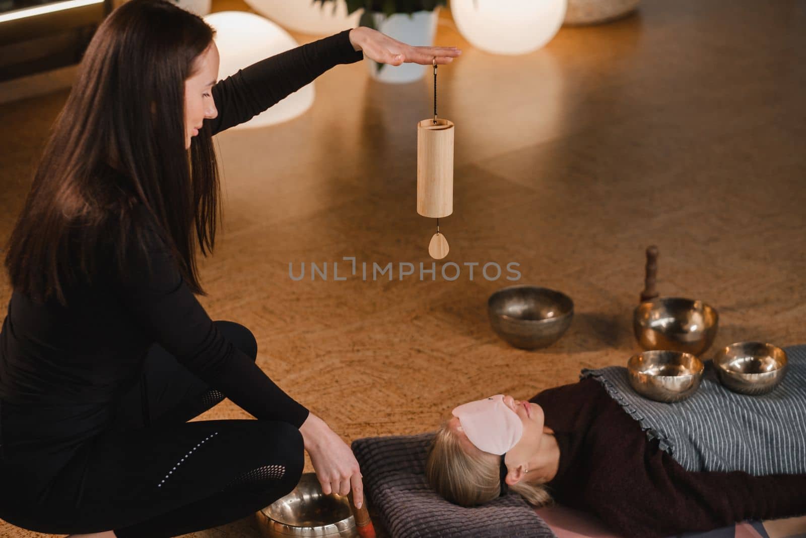 A young beautiful woman is doing a massage with singing bowls and a koshi bell to another girl. Sound therapy.