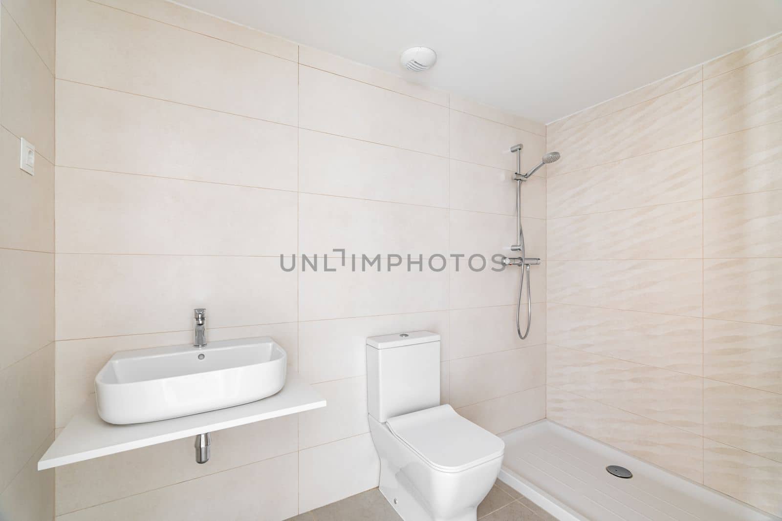 Modern bathroom in white beige tones tile with vanity sink and an open shower in hotel or new apartment. Concept of stylish bathroom interiors with natural light.
