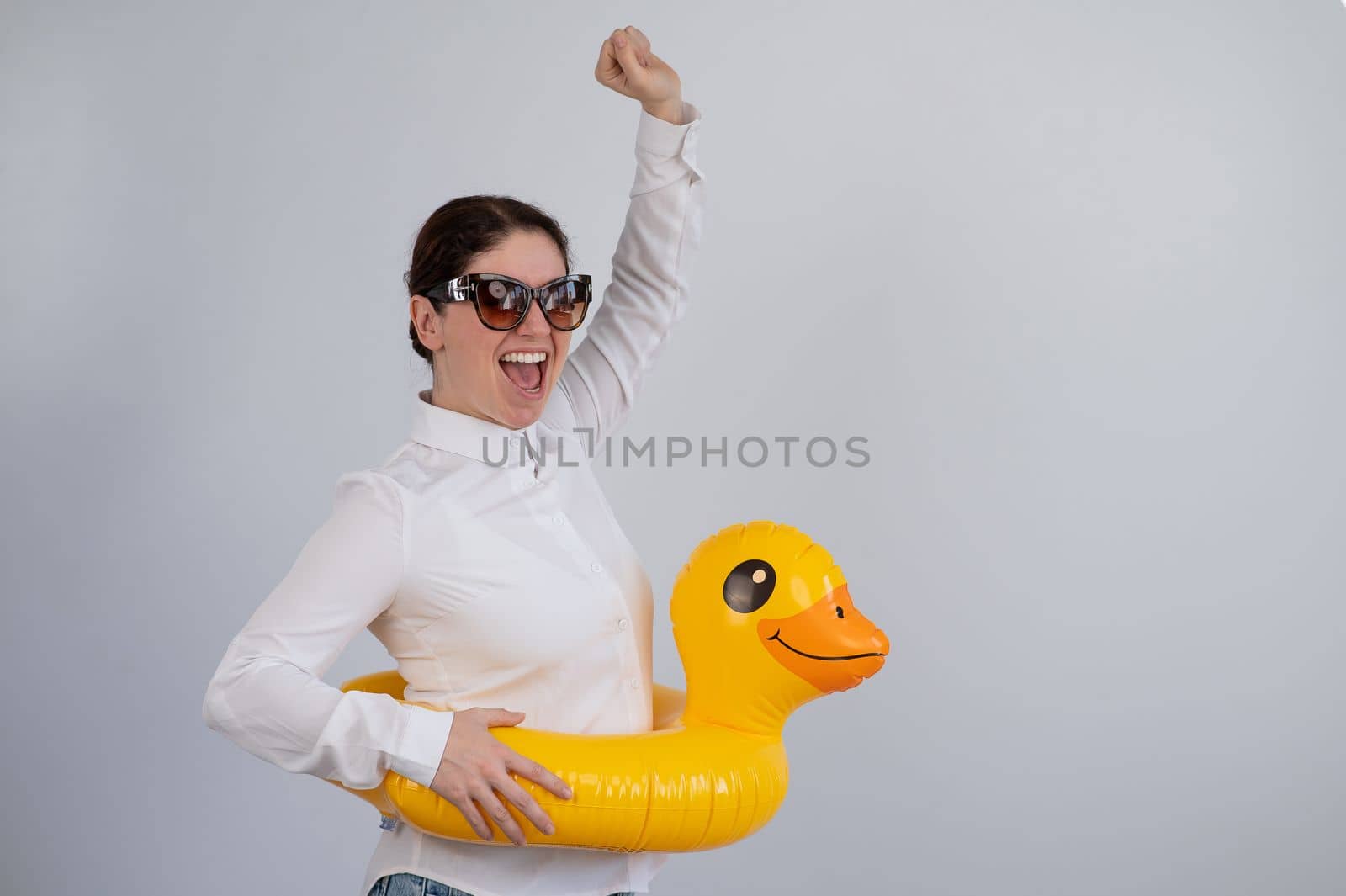 Excited woman in white shirt dreaming about vacation, wearing sunglasses and inflatable duck